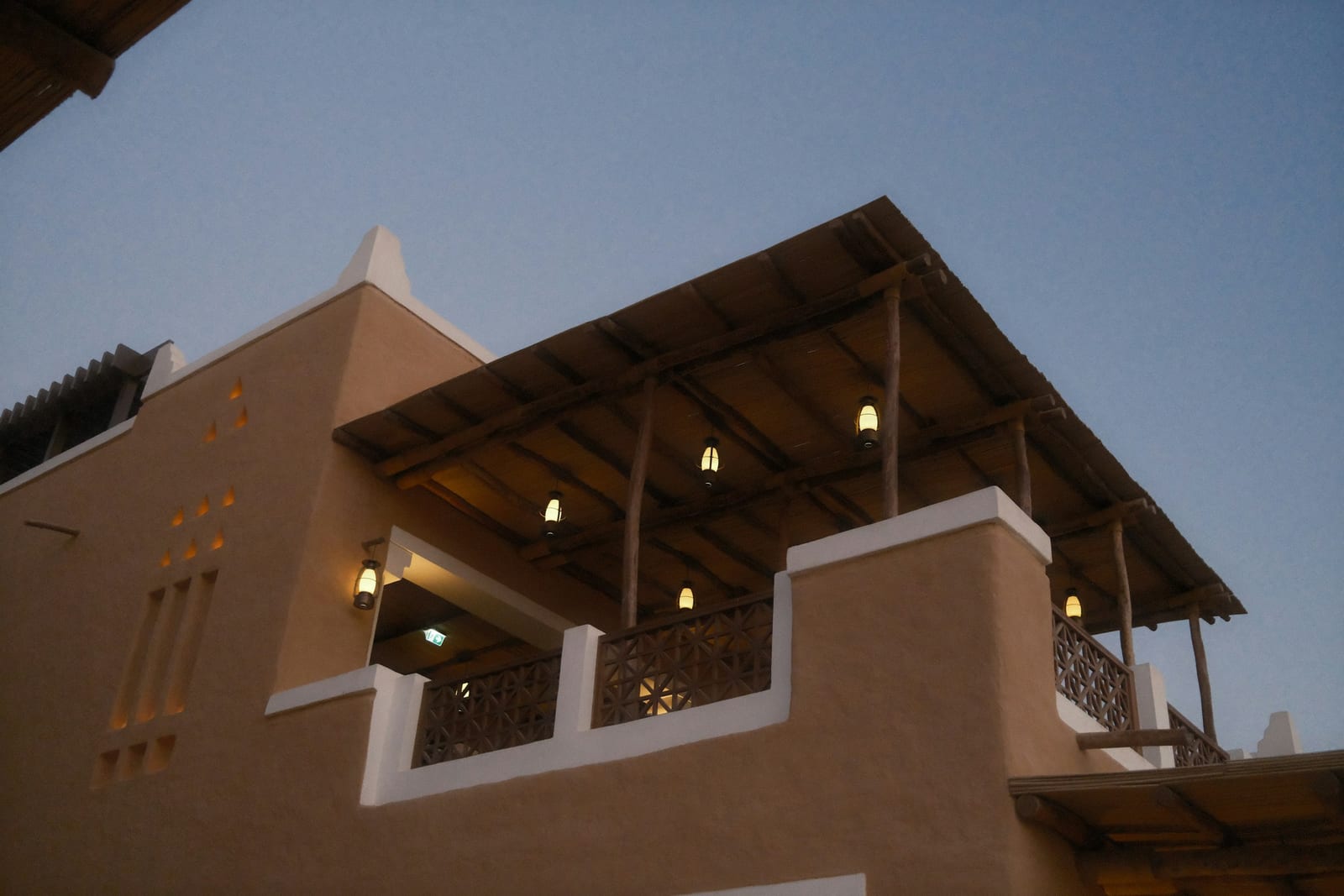 Traditional Diriyah building with a wooden balcony and strings of hanging lights at dusk, June 2026.