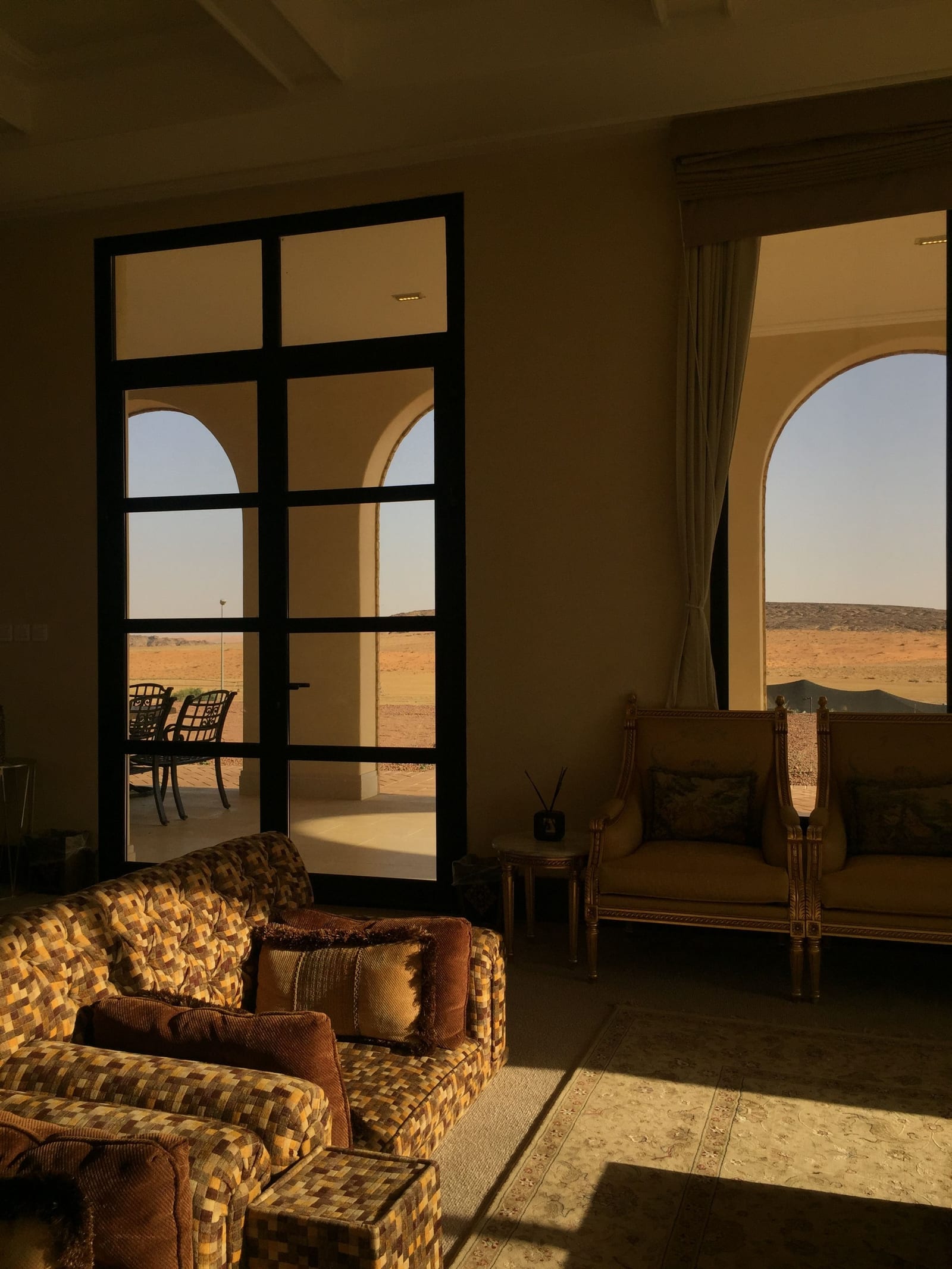 Bright contemporary living room in a Saudi villa in Hail Province with arched windows and desert visible outside.