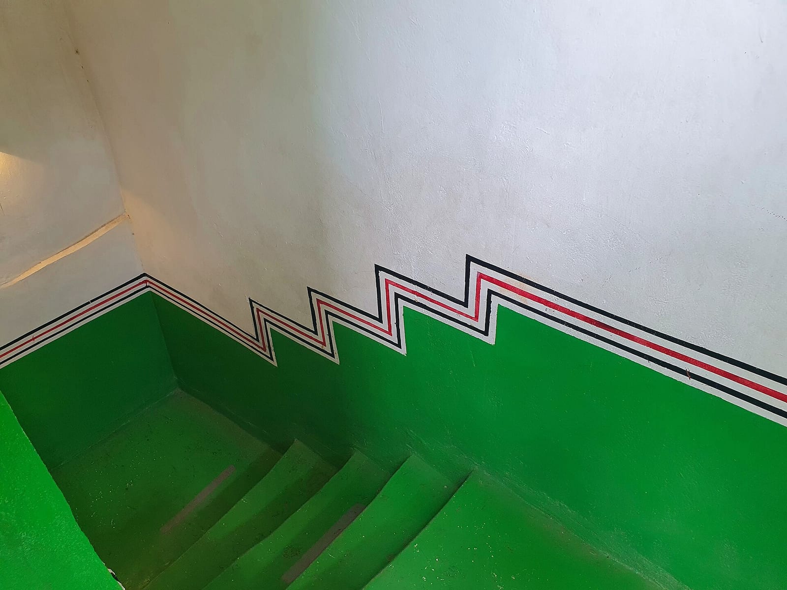 Interior of a traditional stone house in Rijal Alma, Asir, with green walls and painted geometric bands in red, black and white.