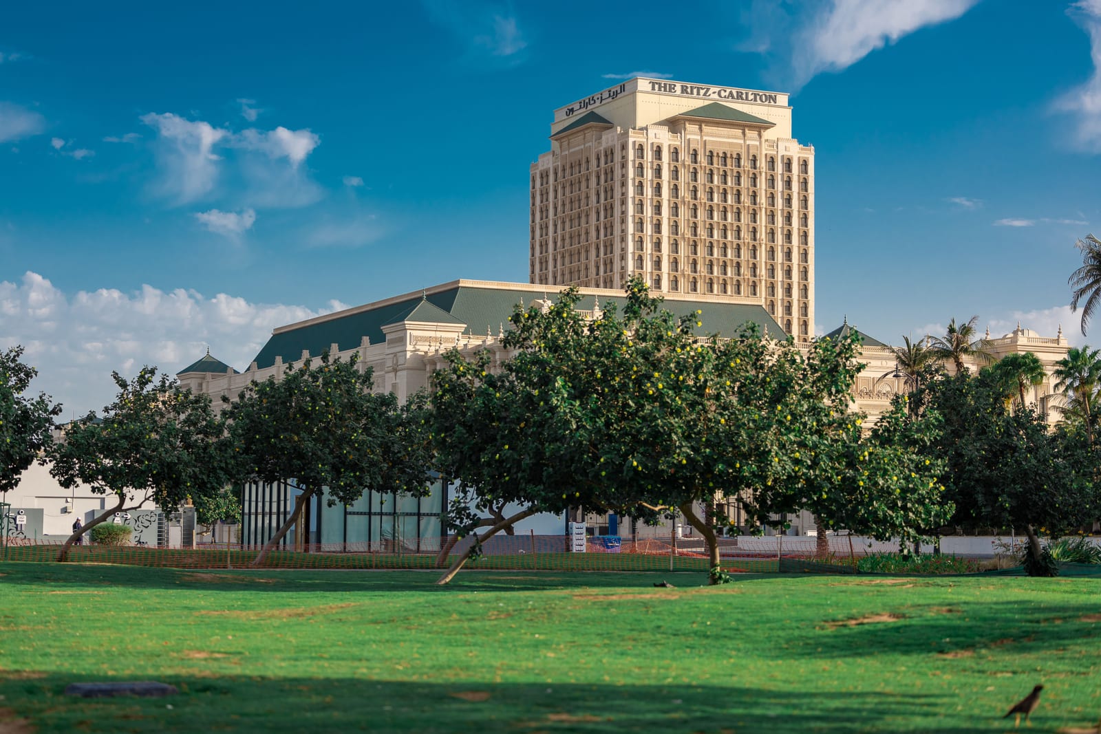 Palace-style exterior of the Ritz-Carlton Jeddah hotel with lawns, mature trees and palms in front.