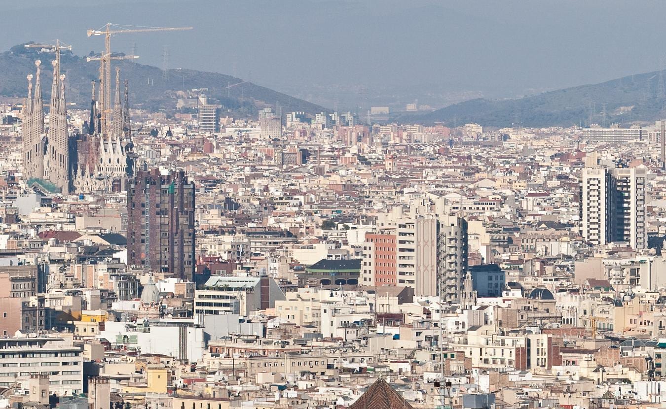 Panorama of Barcelona from Montjuïc, the Eixample grid stretching to Torre Glòries and the sea beyond.