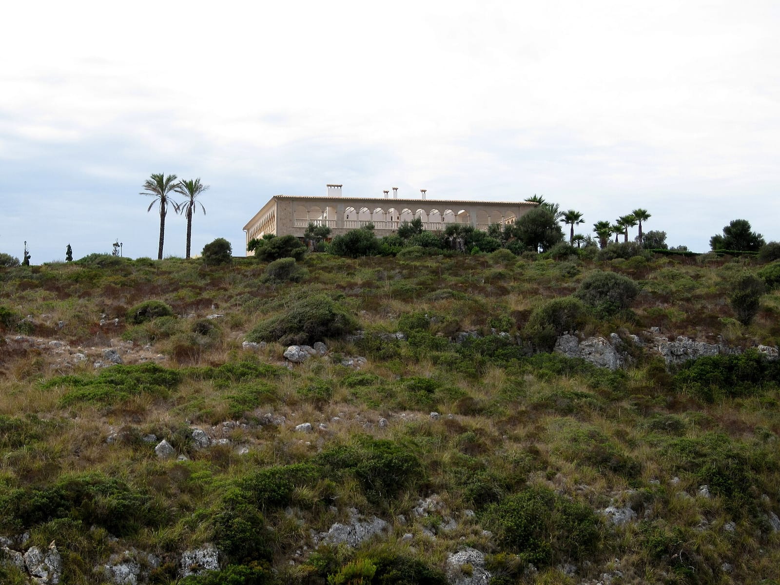 Stone finca above Cala Sequer on the Manacor coast of Mallorca, low sandstone walls under a tiled roof among dry scrub.