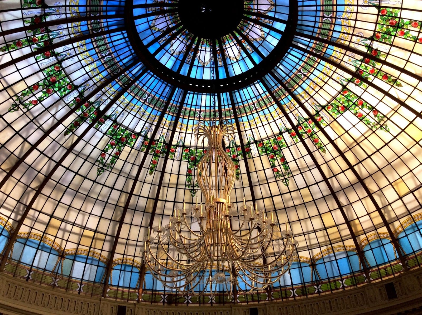 Lounge of the Palace Hotel in Madrid beneath its stained-glass dome, with armchairs and palms in the round hall.