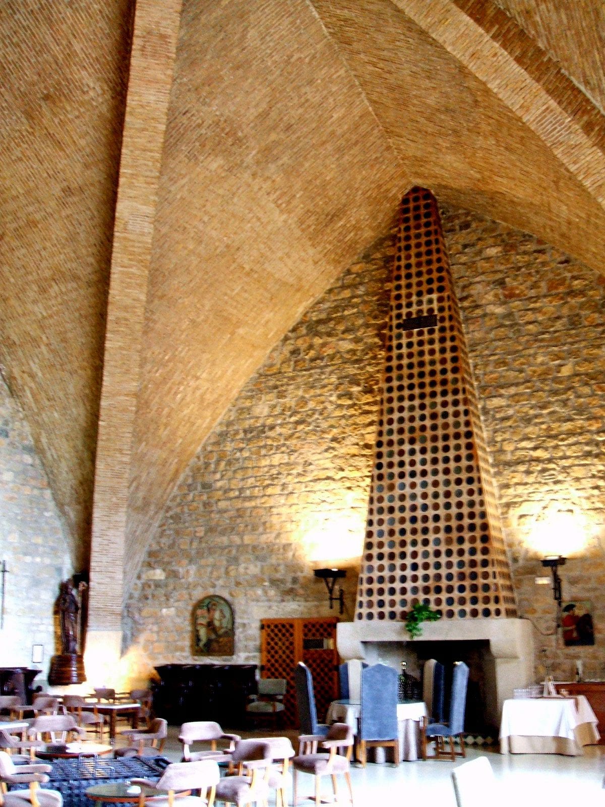 Vaulted stone salón of the Parador of Jaén inside the Castillo de Santa Catalina, with tall arches and heavy furniture.