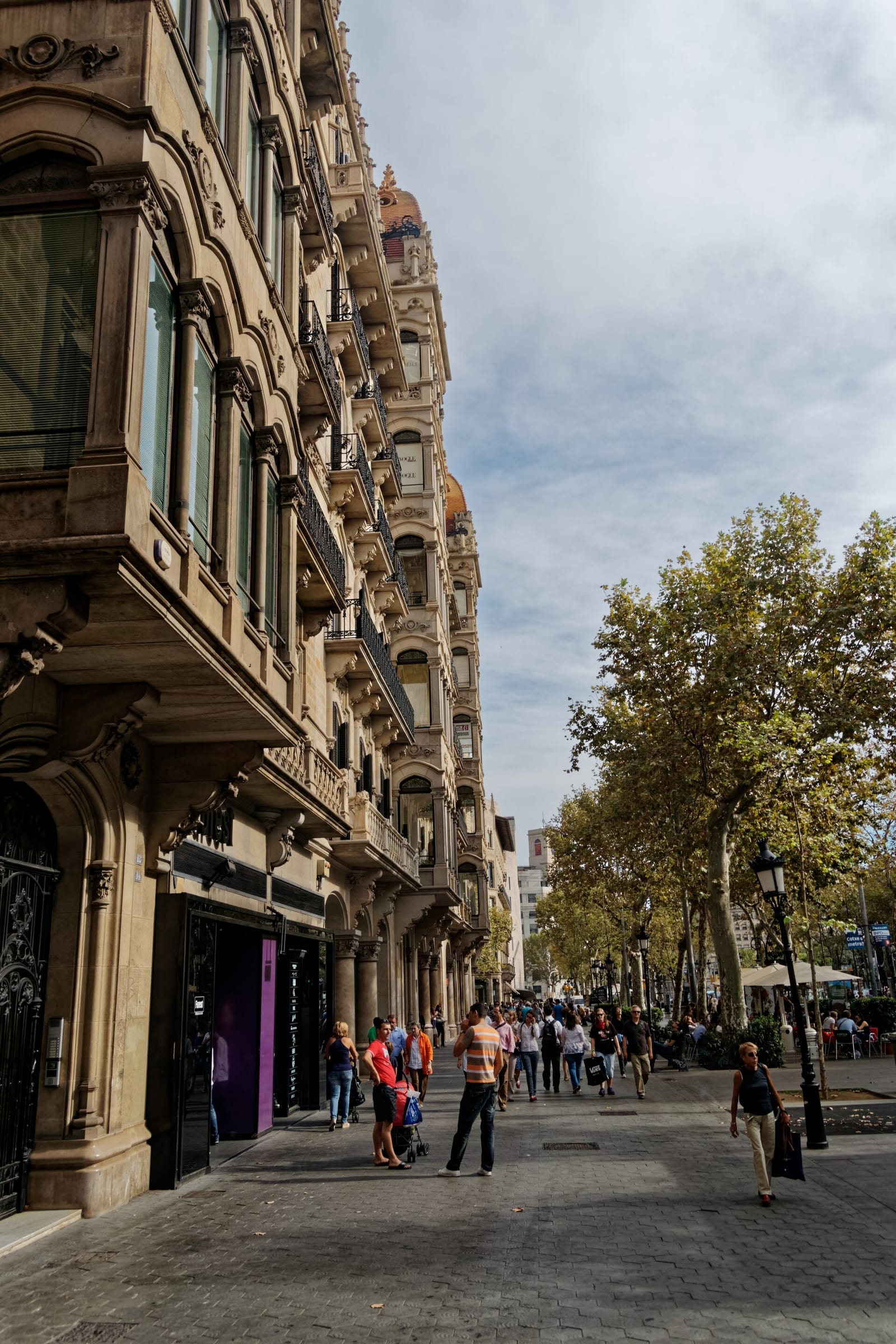 Looking down the Passeig de Gràcia in Barcelona, modernista facades, plane trees and shop fronts along the wide avenue.