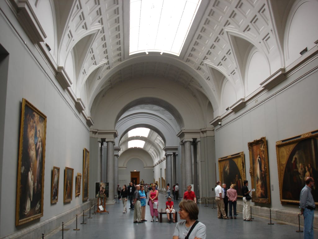 Gallery inside the Museo del Prado in Madrid, large old-master canvases hung on a long wall under a skylight.