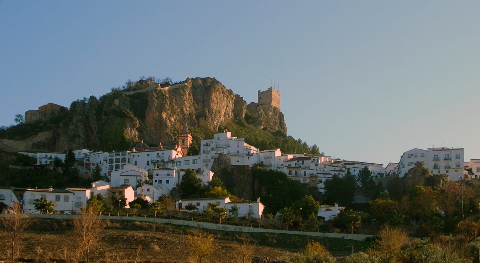 Zahara de la Sierra, a white village in the Cádiz mountains, with terracotta roofs below a rocky crag and a turquoise reservoir.