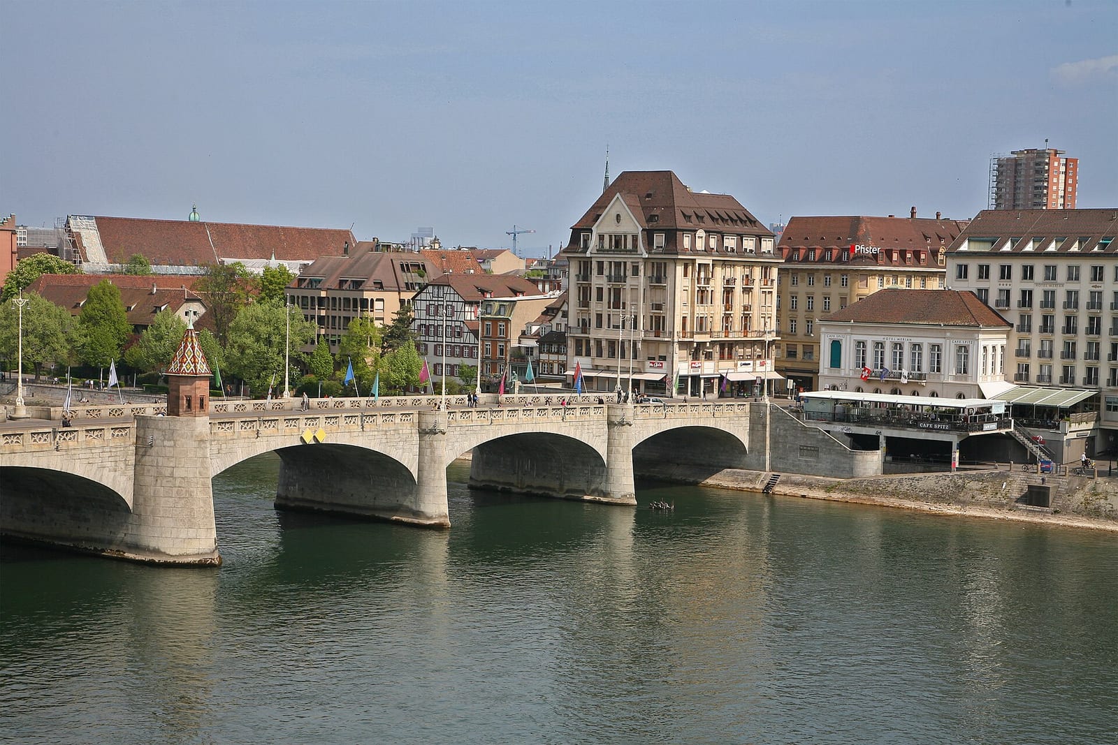 The Mittlere Brücke over the Rhine in Basel with the old-town façades and the Münster tower behind it on a sunny day.
