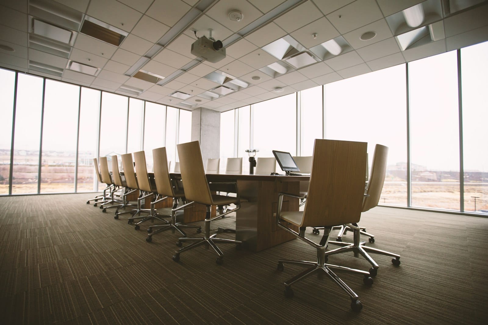 A long boardroom table with leather chairs beside a full-height glass wall looking out over a city.