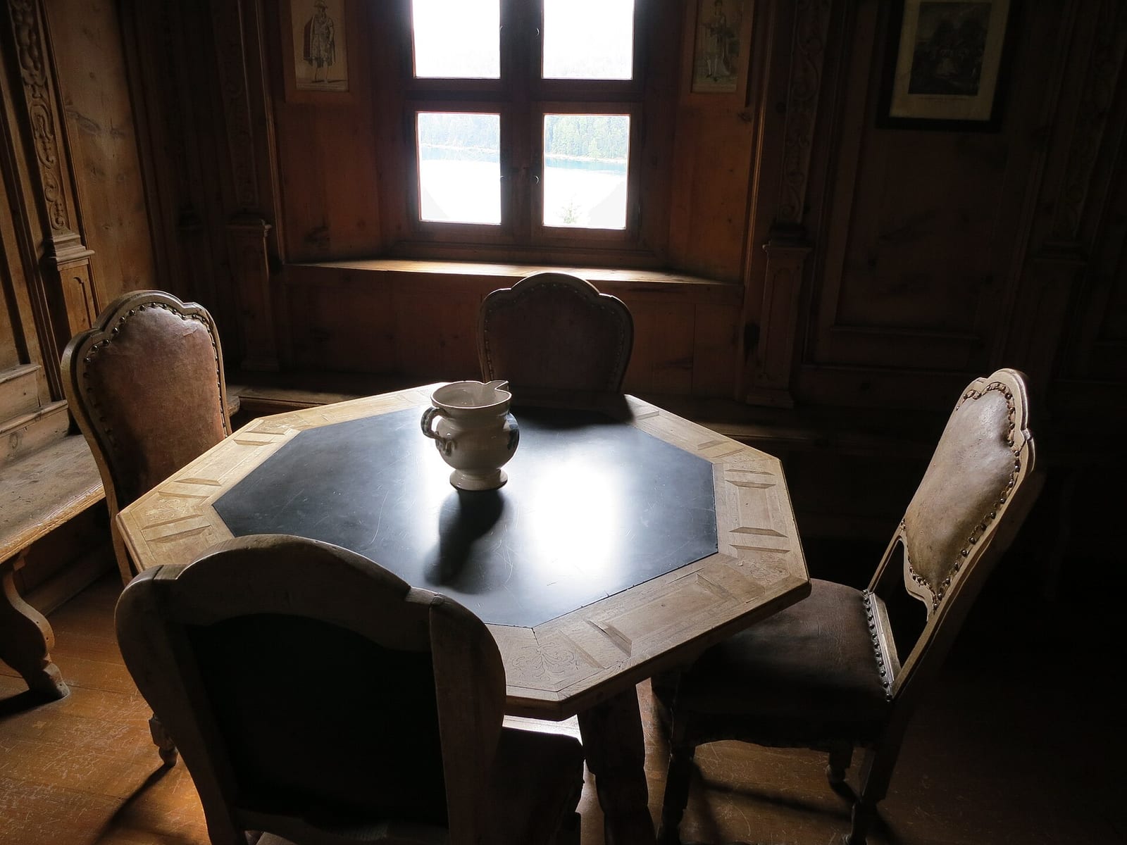 A panelled Engadin Stube in the Engadiner Museum in St. Moritz, with a carved wooden table, chairs and a small window.