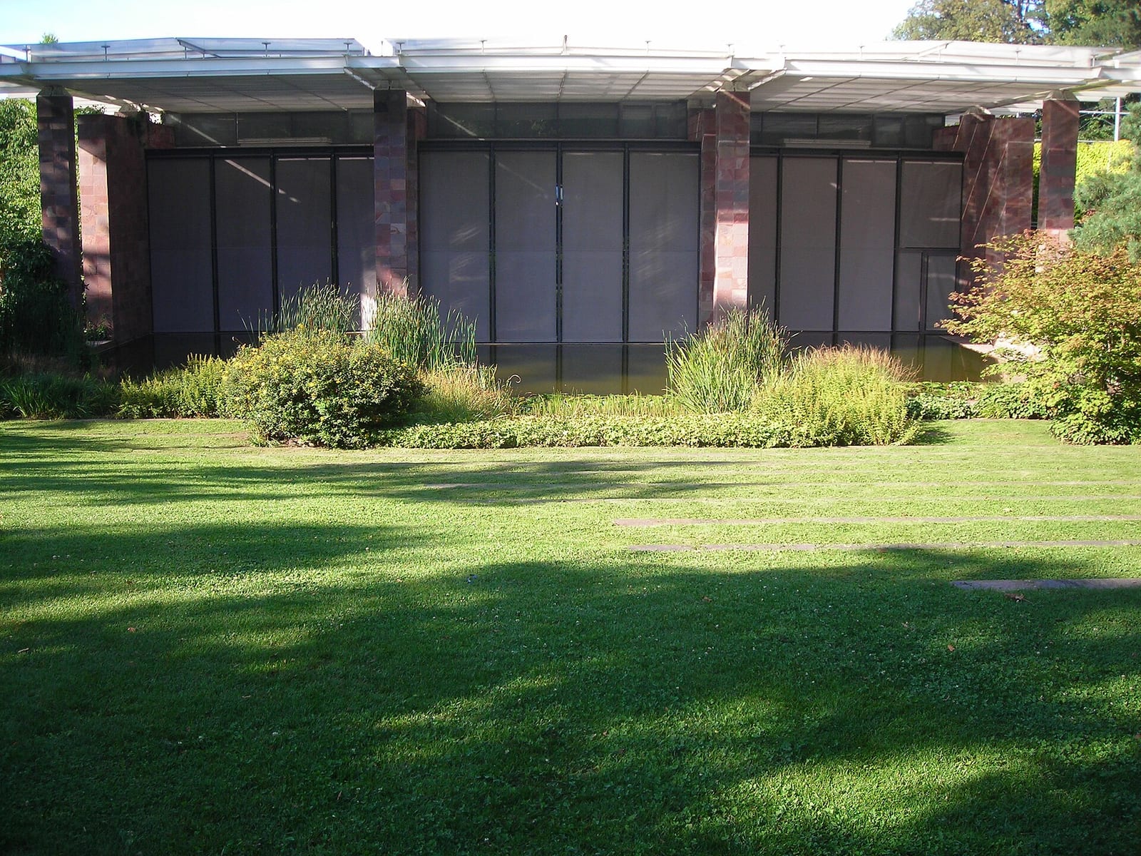 The long glass-and-red-stone pavilion of the Fondation Beyeler in Riehen near Basel set in a lawn with trees.