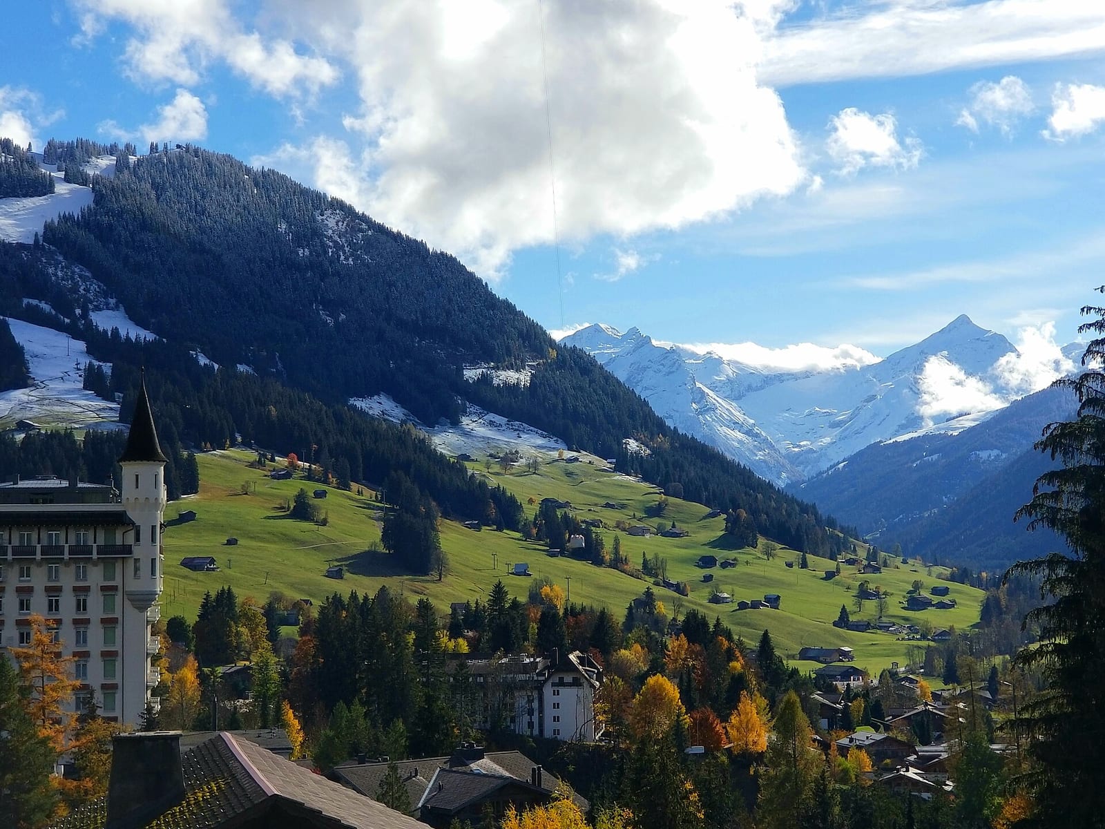 The turreted Gstaad Palace hotel on its hill above the village in summer, with snow-capped Alps in the distance.