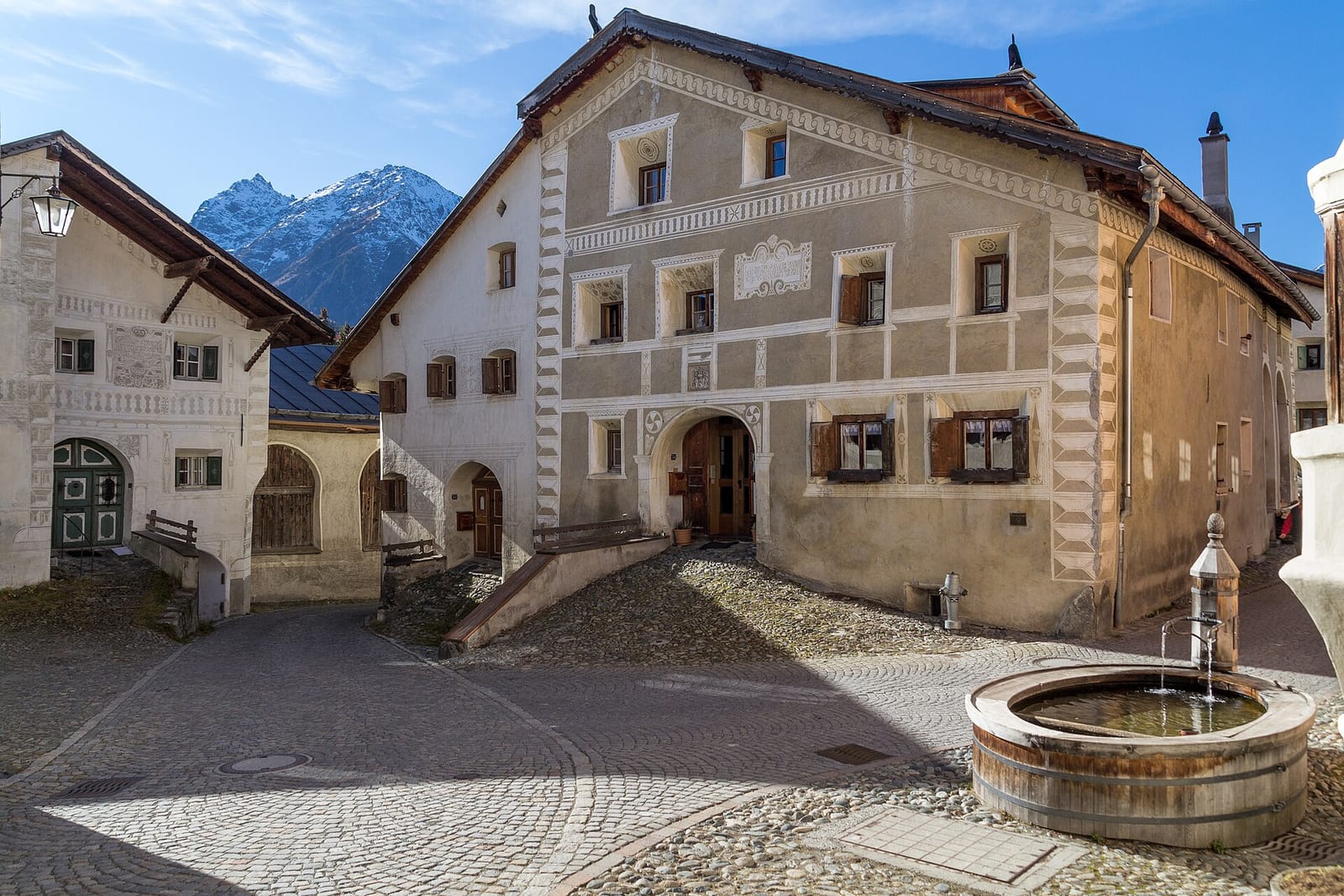 Engadin houses with white sgraffito-decorated façades and a wooden fountain on the village square of Guarda.