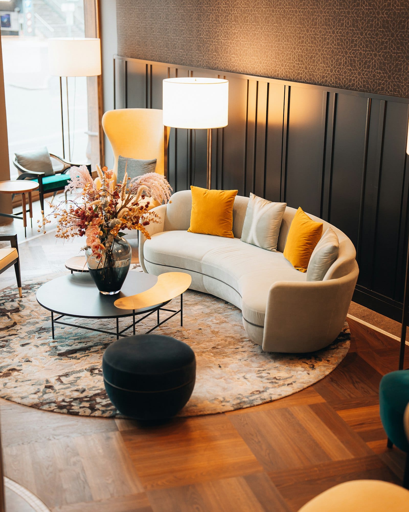 A hotel lounge in Basel with a curved cream sofa, mustard cushions, dark panelled walls and a round rug on parquet.
