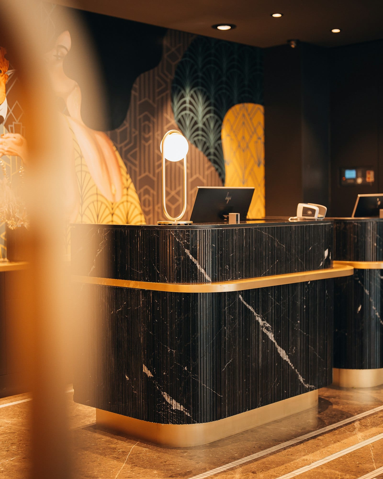 A black marble reception desk with brass trim and a patterned wall in the lobby of the Hotel Märthof in Basel.