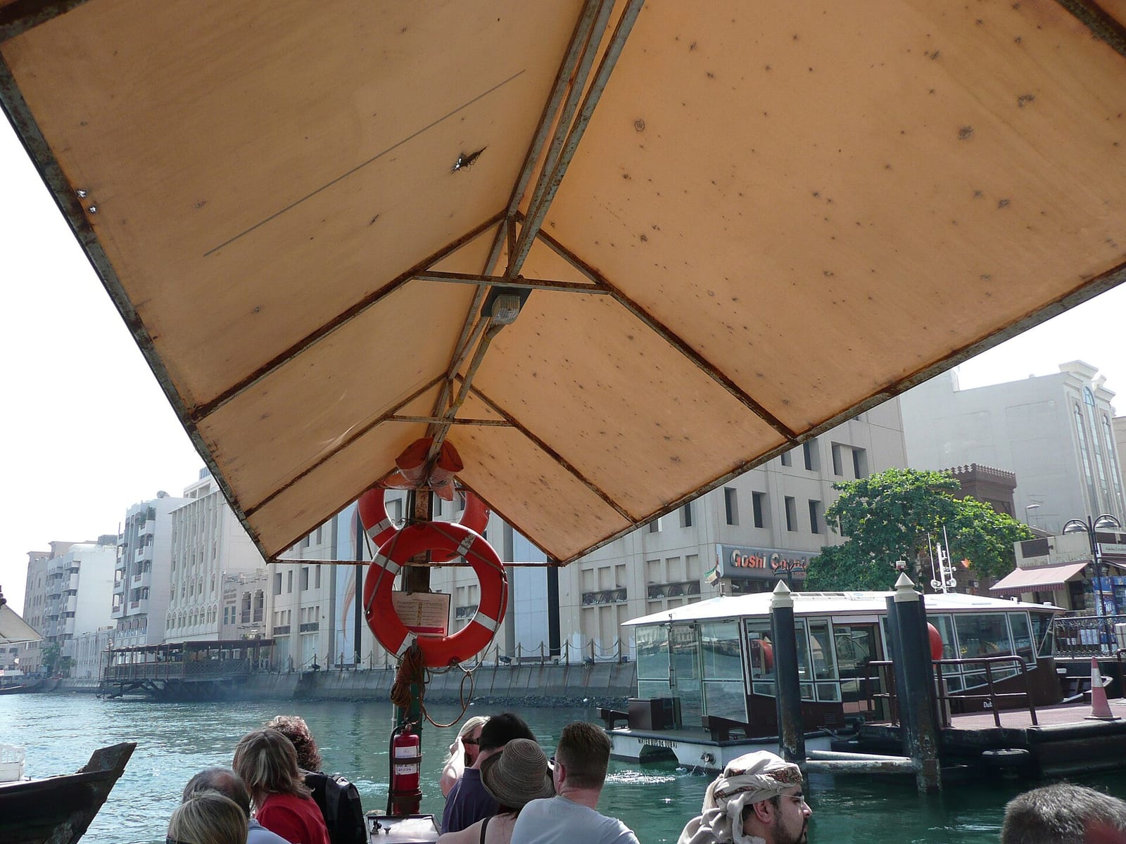 Dubai Creek seen from a traditional wooden abra water taxi, with dhows and the low buildings of Deira along the far bank.