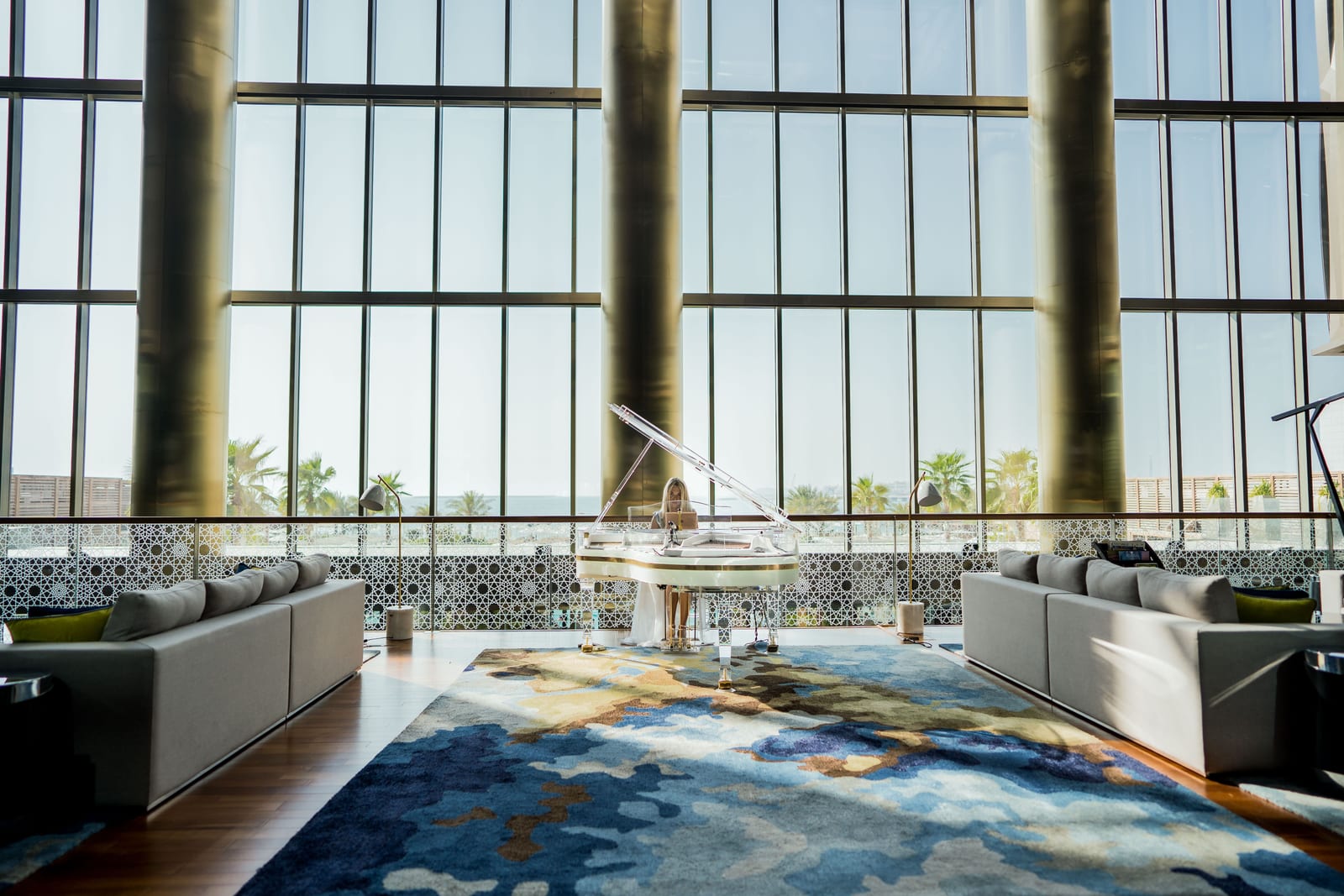 Modern Dubai hotel lobby with a grand piano, plush sofas, a large rug and tall windows letting in daylight.