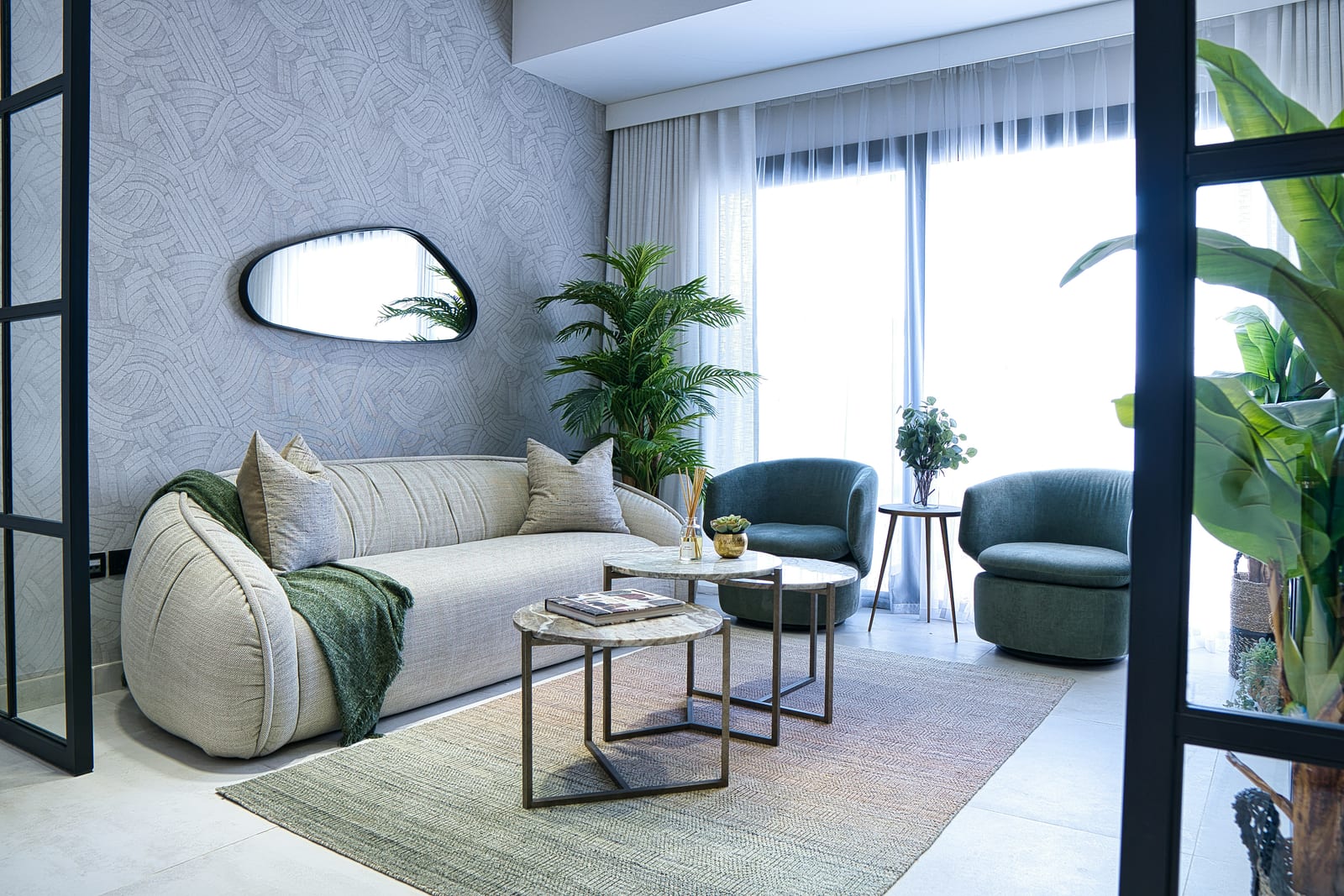Modern Dubai living room with a plush cream sofa, green velvet chairs, a marble coffee table and a large blank wall behind.