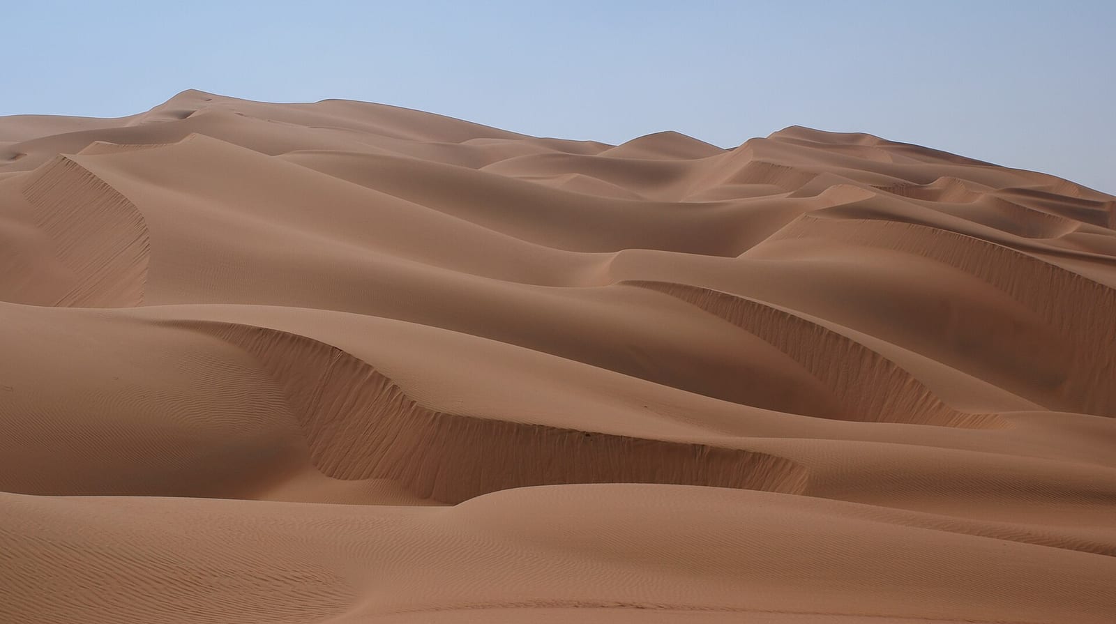 Wind-sculpted red-orange sand dunes of the Rub' al Khali in the Liwa region of Abu Dhabi emirate under a clear sky.
