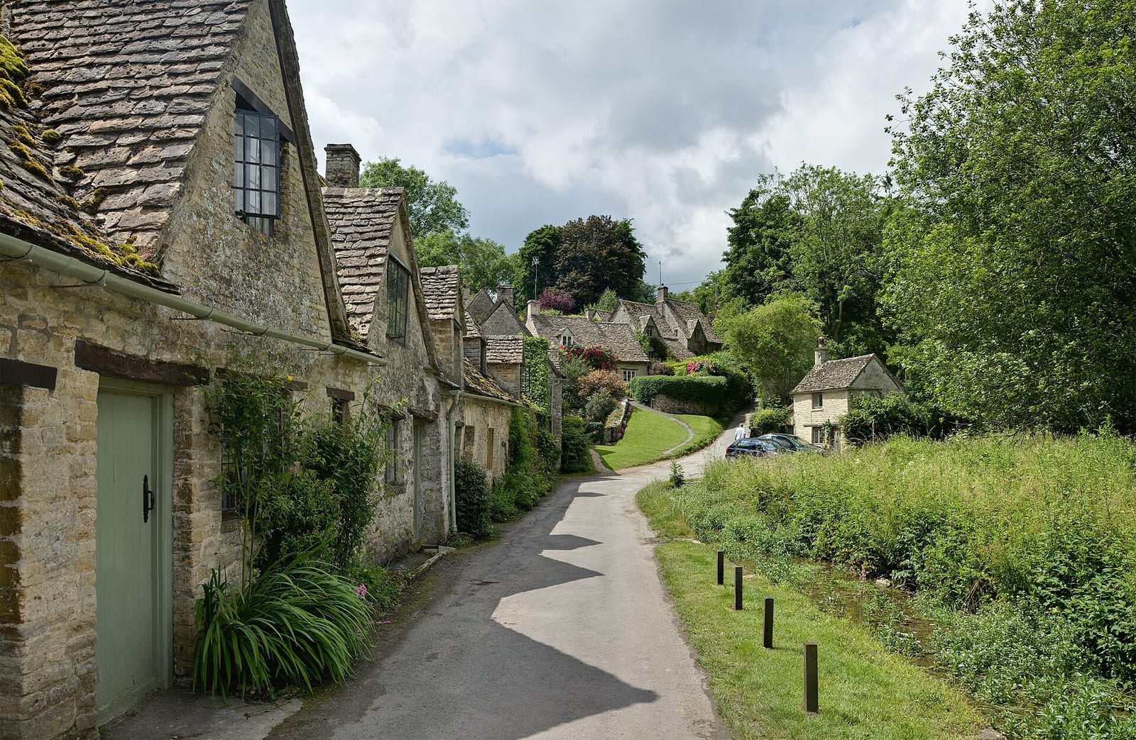 Honey-coloured stone cottages of Arlington Row, Bibury, in the Cotswolds beside a stream.