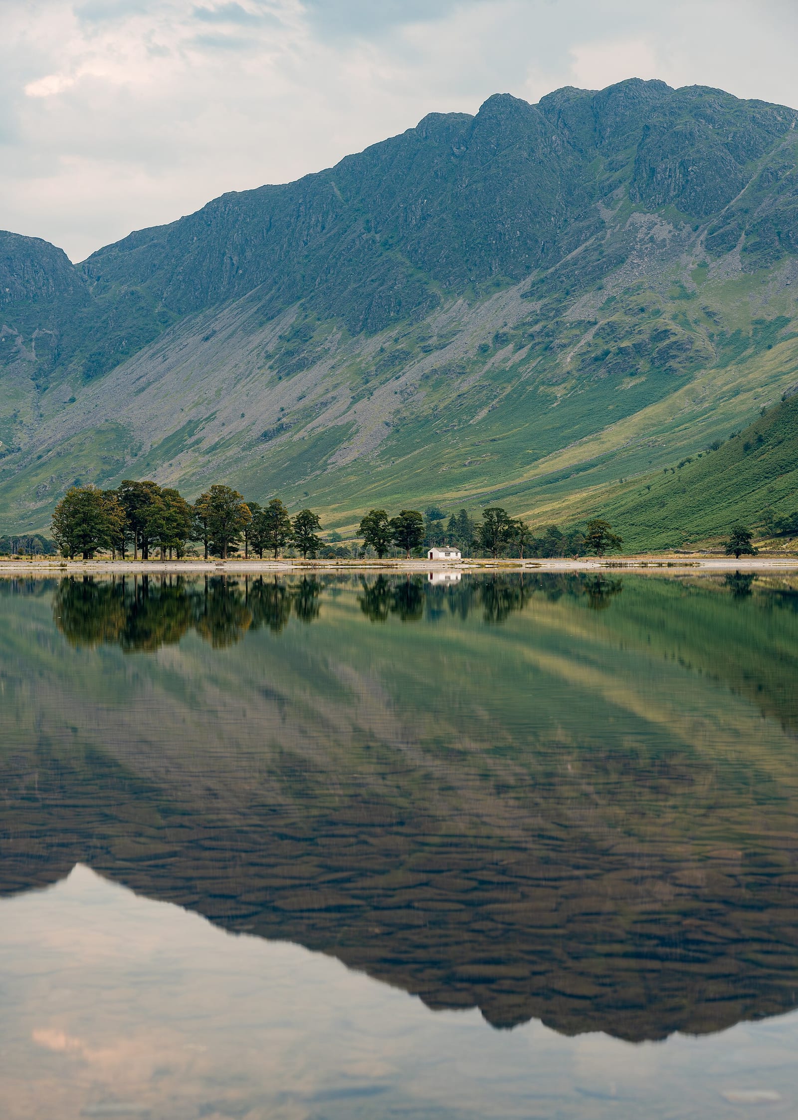 Buttermere lake in the Lake District with the fells of Haystacks behind under a cloudy sky.