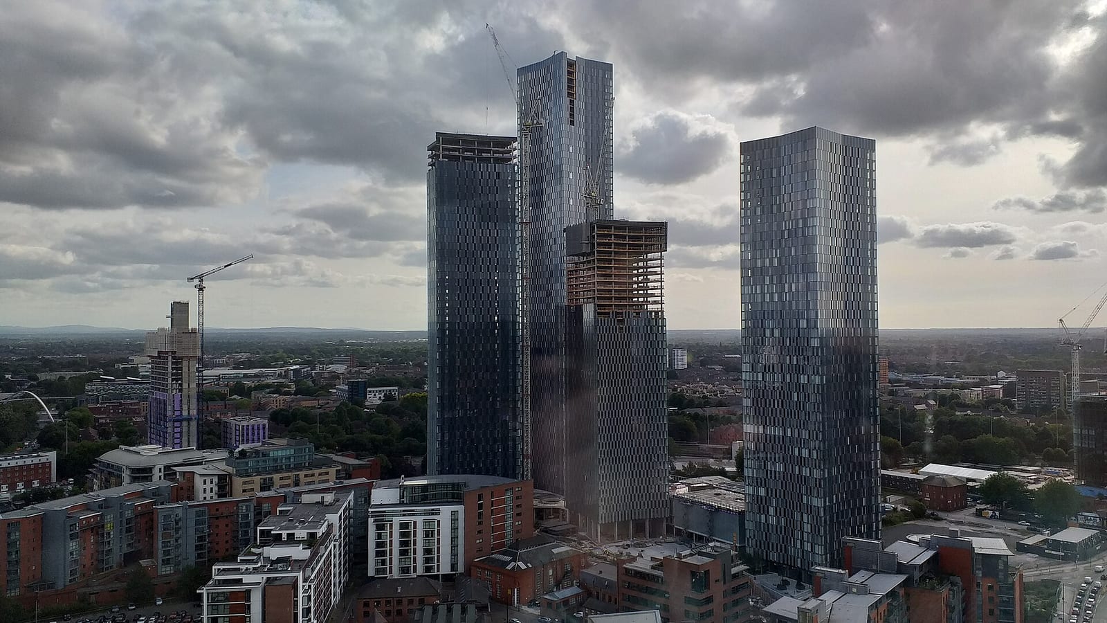 The four Deansgate Square residential towers on the Manchester skyline against a blue sky.