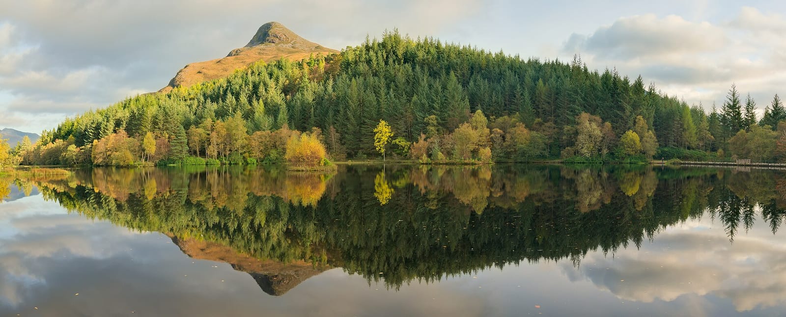 Panoramic reflection of autumn trees and the Pap of Glencoe in the still water of Glencoe Lochan.
