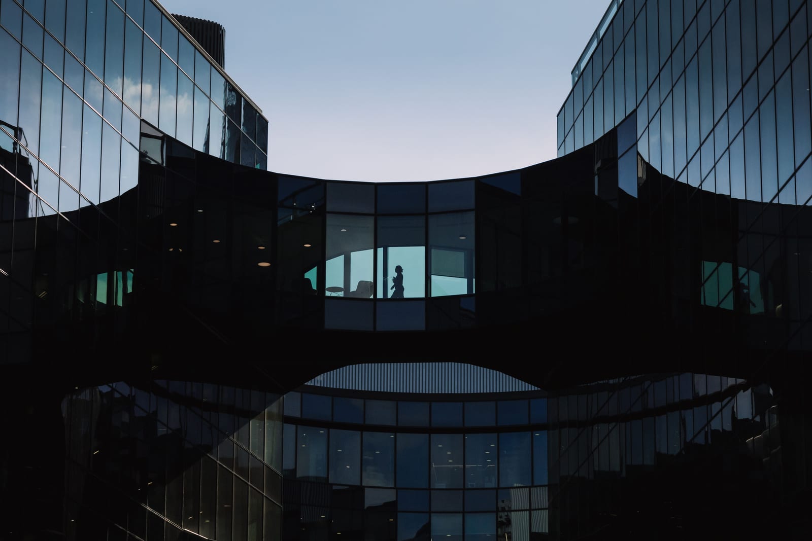 Contemporary glass office buildings in London linked by a skybridge with silhouetted people.