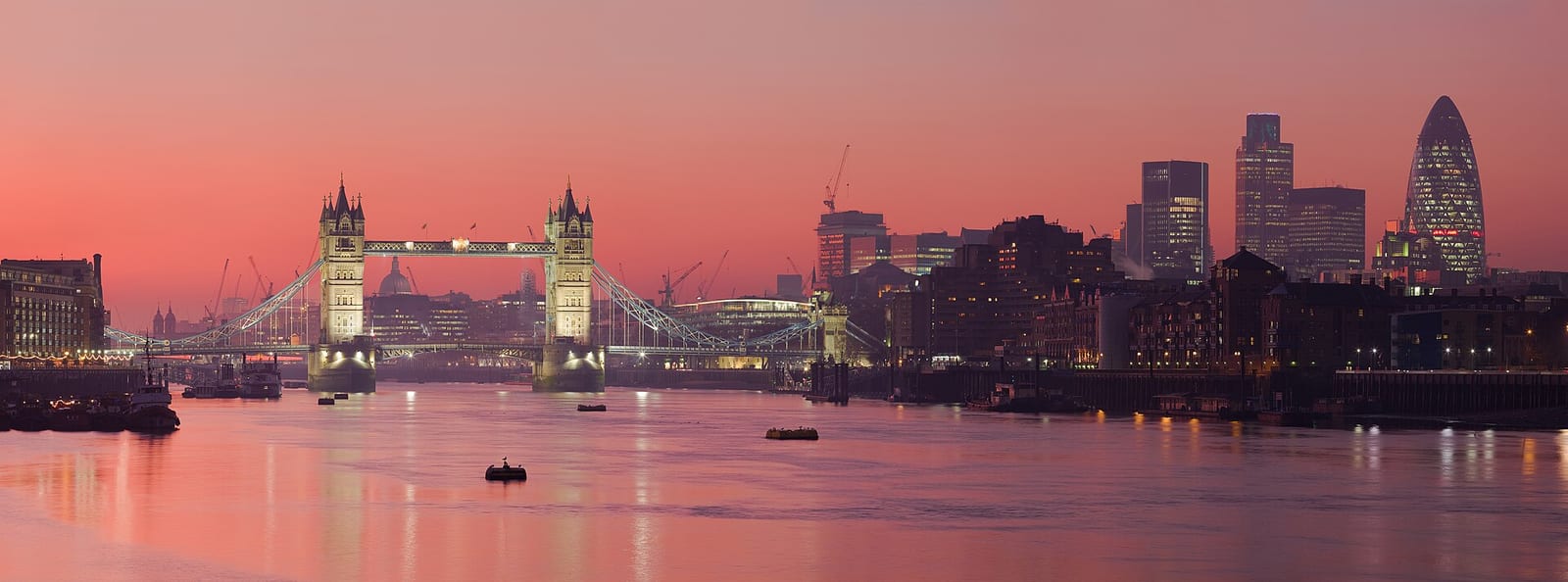 Panoramic view of the London skyline across the Thames at sunset, Tower Bridge and the City towers behind.