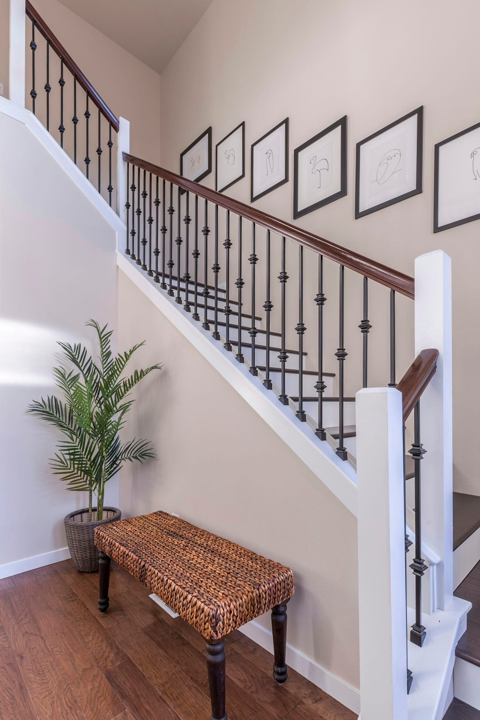 White entry hall with a straight staircase, black handrail and a wooden bench below the stairs.