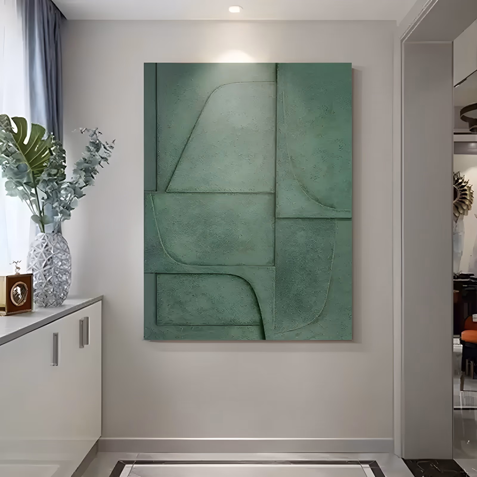 a large vertical plaster relief painting in a single sage green, its surface divided into flat panels by curved and straight raised edges that catch light along each ridge, with a chalky matte finish