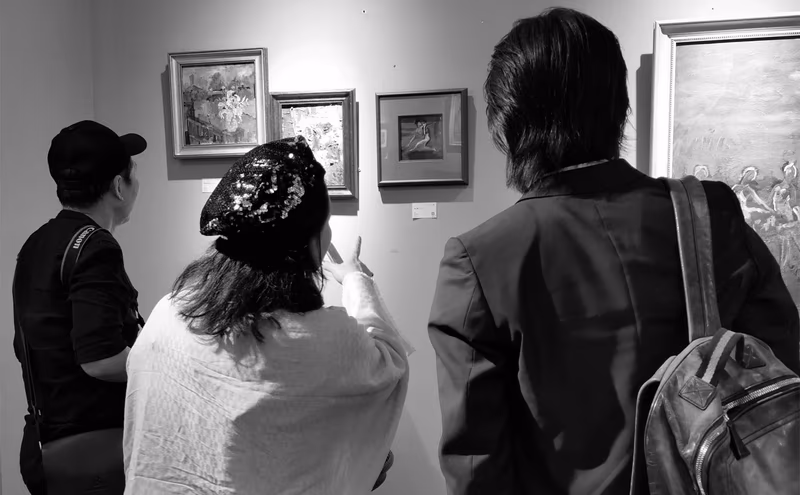 Three visitors standing in front of a wall of framed paintings at a Siji Art Hub exhibition, photographed in black and white